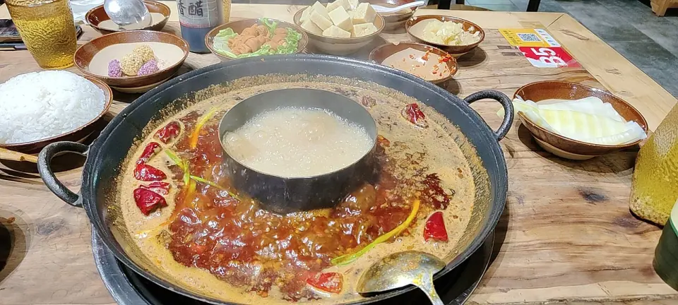 Sichuan-style hotpot with red chili broth, vegetables and side dishes on a dining table